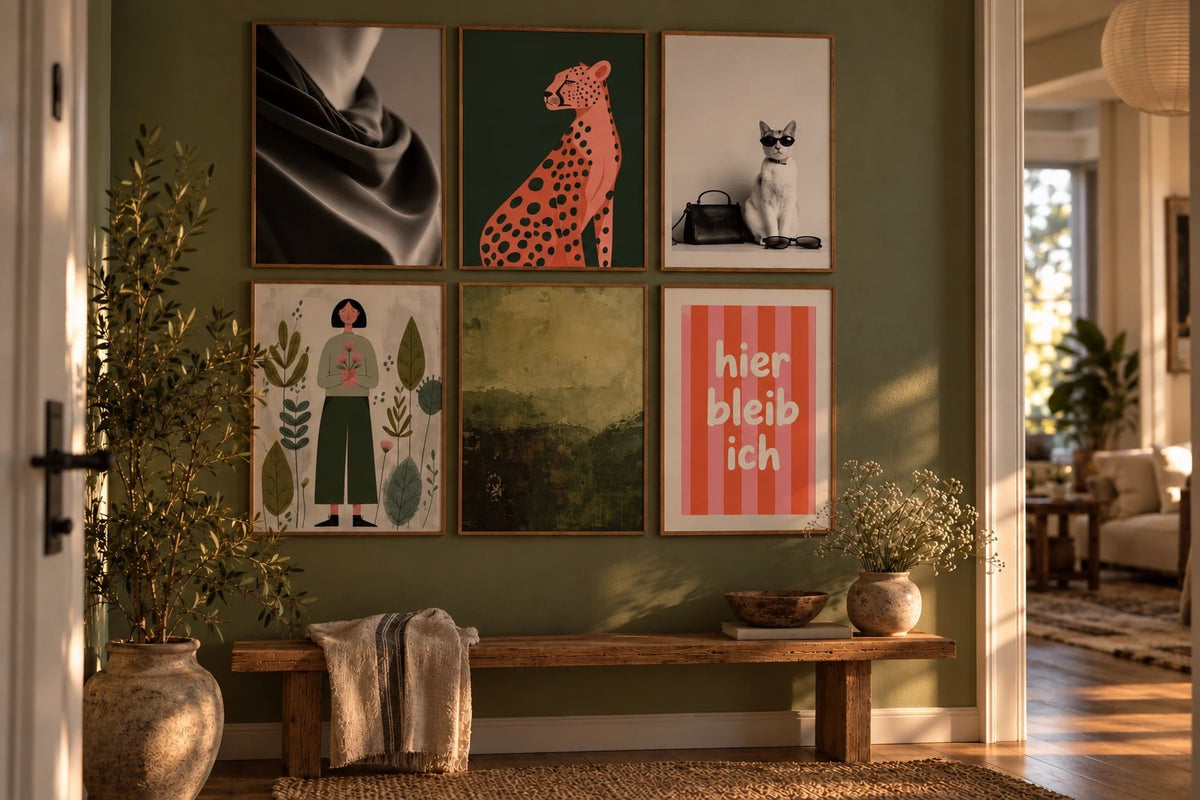 Bunte Bilderwand im Flur: sechs Poster im Raster über einer Holzbank, Stofffalten, rosa Gepard, Katze mit Sonnenbrille, Frau mit Blumen, olivgrüne Landschaft und Schriftzug hier bleib ich